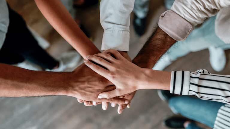 Top view of people holding hands together while standing in the office.