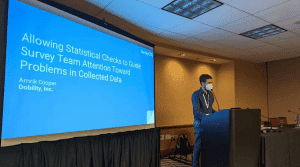 A presenter on-stage, in front of a screen that reads: Allowing Statistical Checks to Guide Survey Team Attention Toward Problems in Collected Data