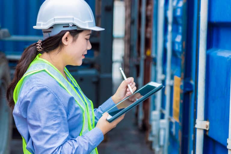 A young woman in a white hard hat uses electronic data capture software on a tablet.