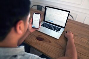 A picture of how to analyze data from a survey, showing a man holding a mobile device and sitting in front of a laptop. He is using both devices for data analysis.