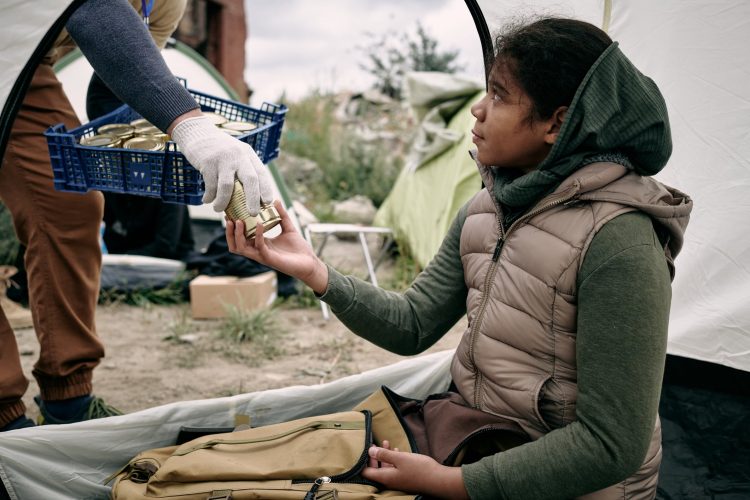 Girl in a refugee camp receives food from aid worker.