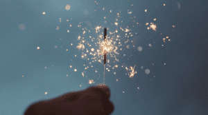 Hand holding a sparkler against a blue sky.