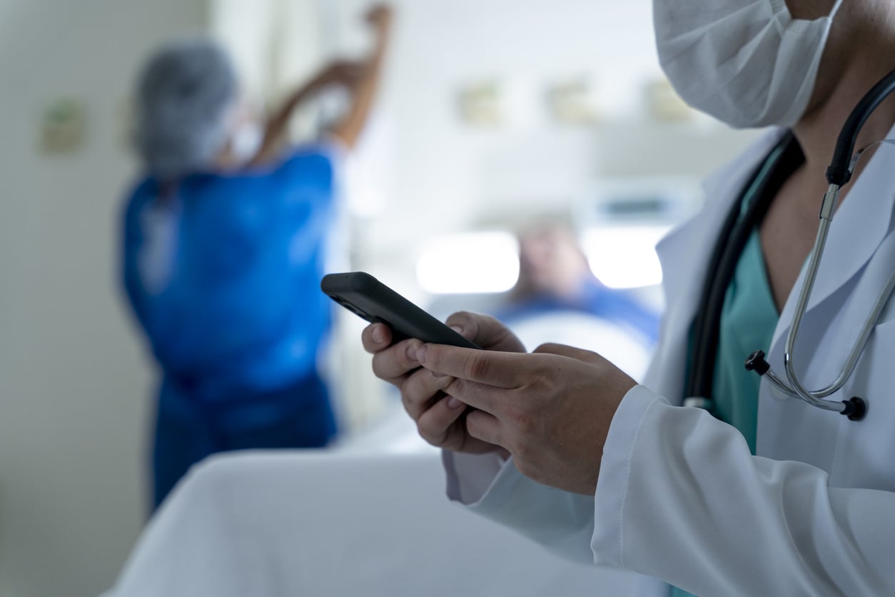 Doctor looking at patient chart on cell phone while patient is lying on a stretcher being medicated by nurse