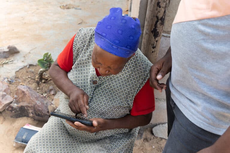 An African woman inspects a mobile device with the help of a volunteer.